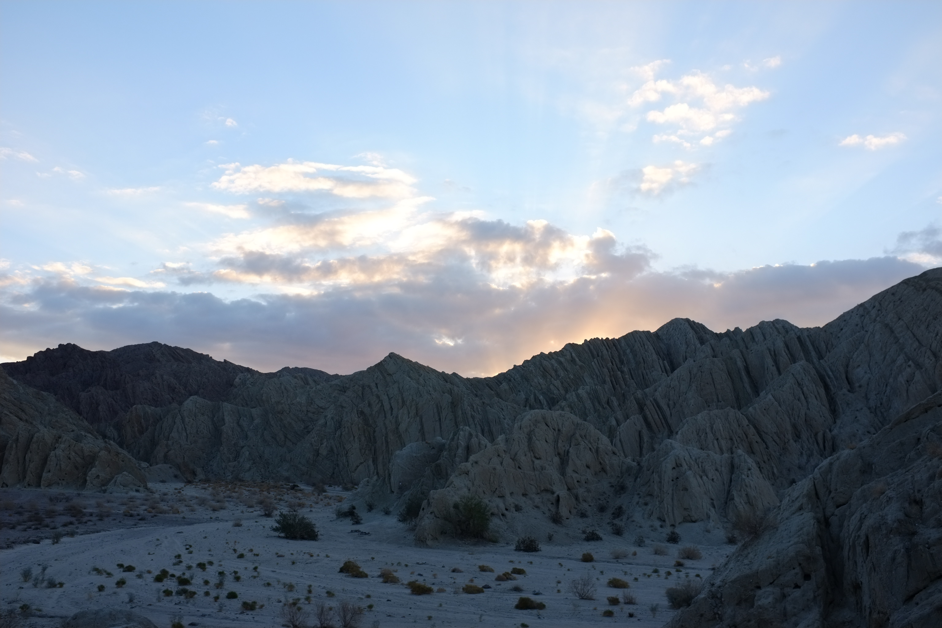 Dramatic desert landscape with jagged mountain ridges under a colorful sunset sky.